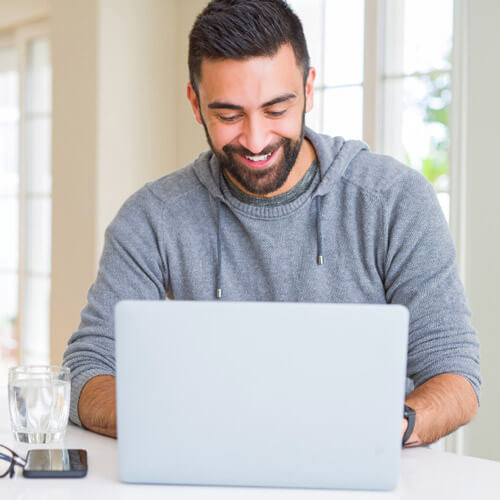 A man happily working on his laptop, smiling as he types on the keyboard.