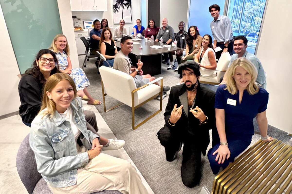 A lively office meeting with people seated in a semi-circle, engaging in discussion. The environment looks relaxed yet professional, with natural light and modern furniture.