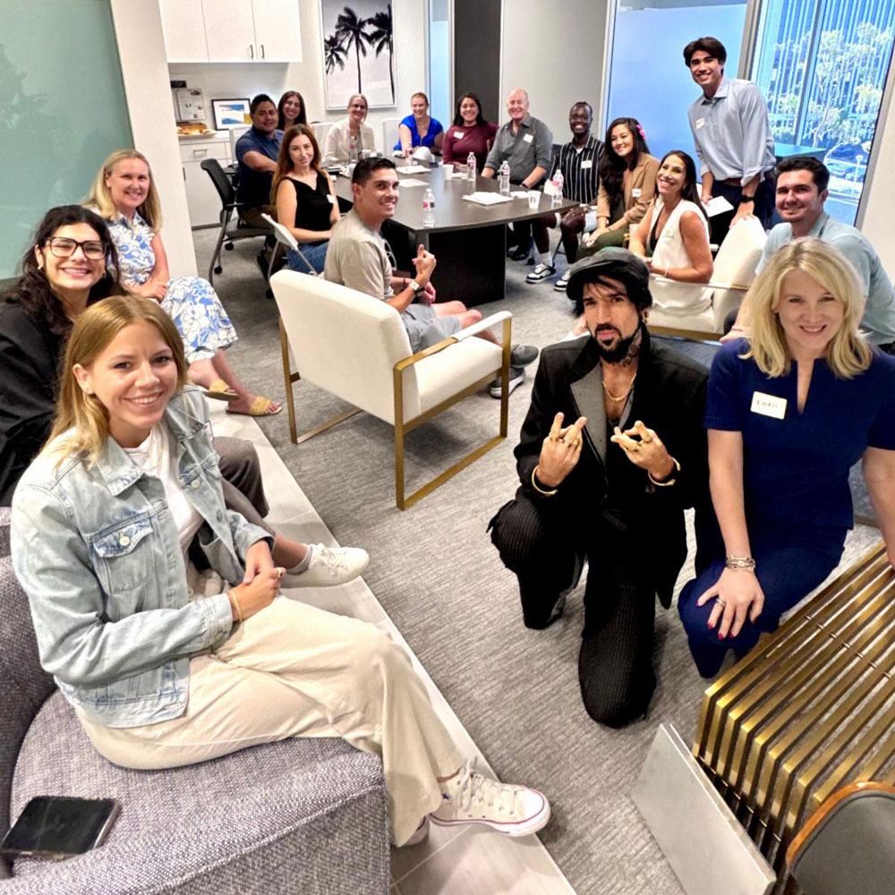 december_newsletter_2025_10 A large group of people sit together in a conference room smiling for a group photo during a meeting or event.