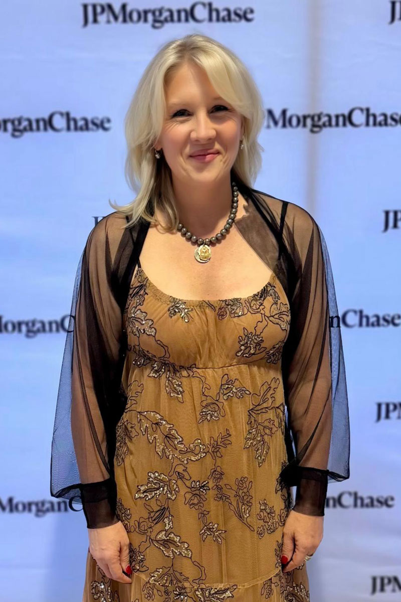 december_newsletter_2025_4 A woman in a tan floral dress stands smiling in front of a JP Morgan Chase backdrop.