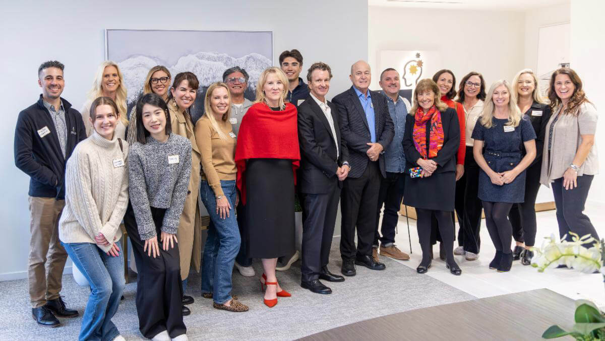 A group of attendees pose together at a Neurologics event, smiling in a bright indoor setting.