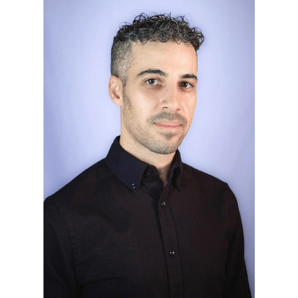 A headshot of a man with short curly hair wearing a black shirt, posed against a light background.