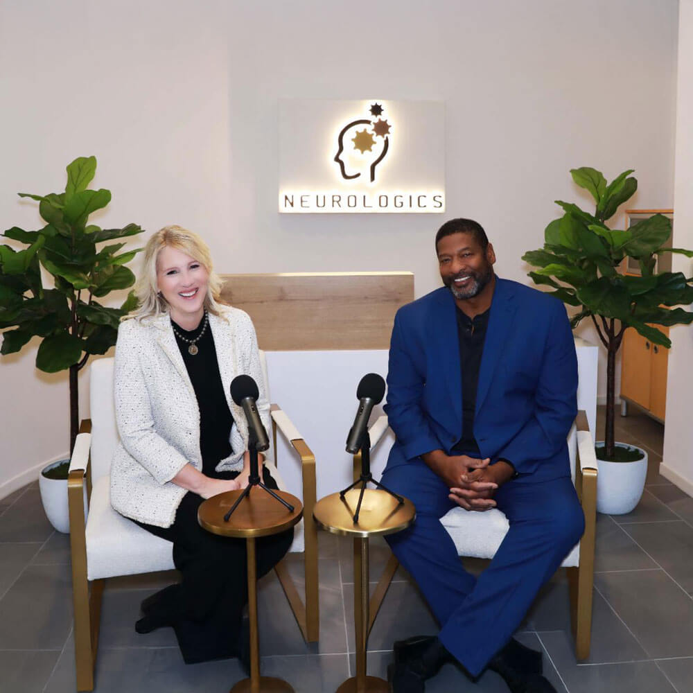 april_newsletter_2026_2 Two smiling people — a woman in a white blazer and a man in a blue suit — sit in armchairs with podcast microphones in front of the illuminated Neurologics logo in a modern clinic reception area.