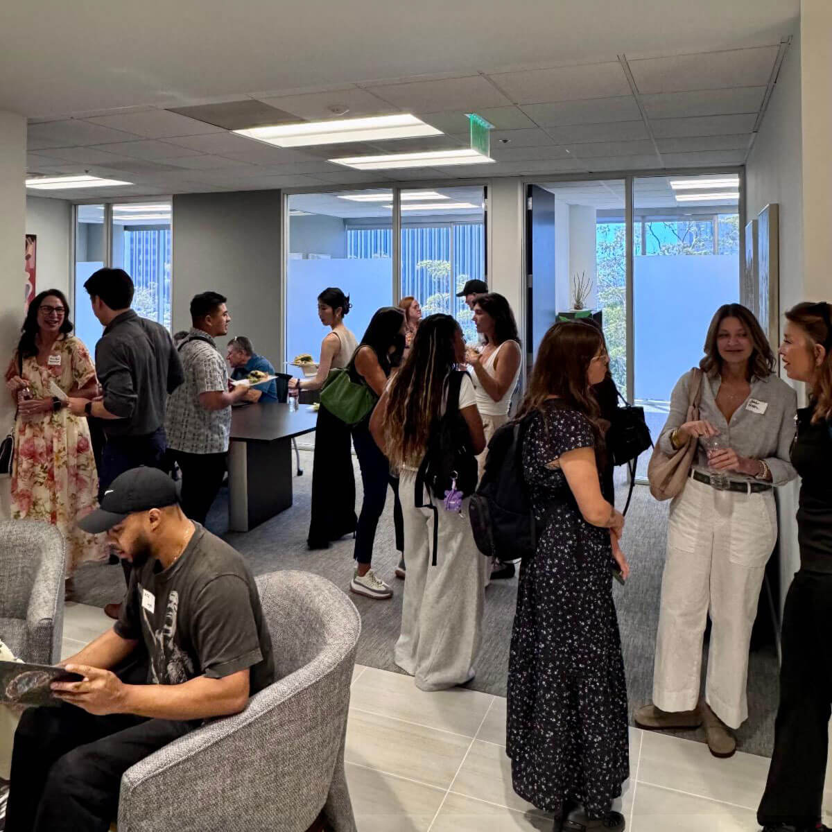 Several small groups of people stand around chatting and networking in a brightly lit office corridor during an event.