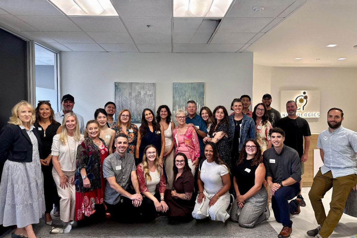 A large group of smiling attendees posing together for a group photograph in the reception area of a Neurologics office.
