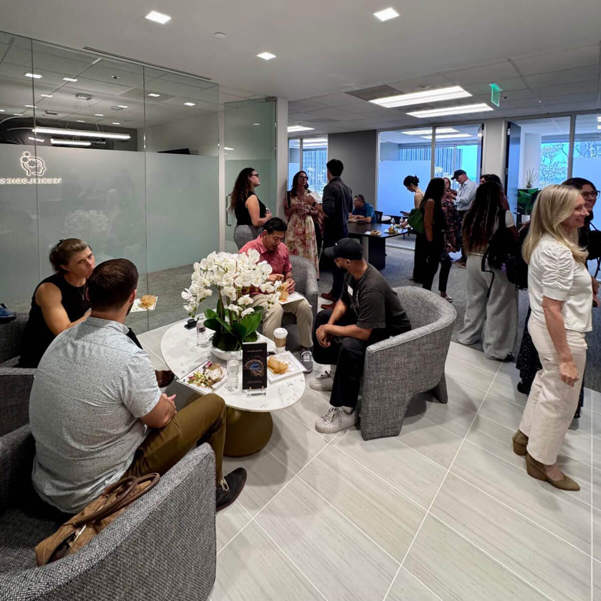 Attendees mingle, chat, and enjoy a catered lunch in a modern Neurologics office lounge area during a networking event.
